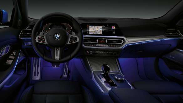 BMW Série 3 Berline, éclairage d'ambiance. Vue de face du poste de conduite côté conducteur de la BMW Série 3 Berline avec espace aux pieds baigné de lumière bleue diffusée par l’éclairage d’ambiance