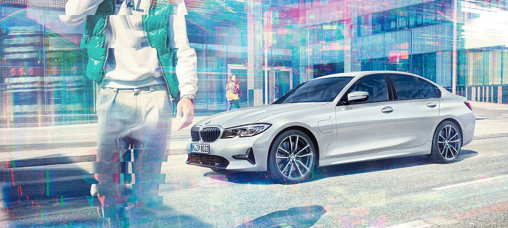 BMW Série 3 Berline, vue latérale BMW 330e iPerformance. Vue à trois-quarts latérale de la BMW 330e iPerformance Berline à l'arrêt devant un bâtiment en verre et passants dans une ville.
