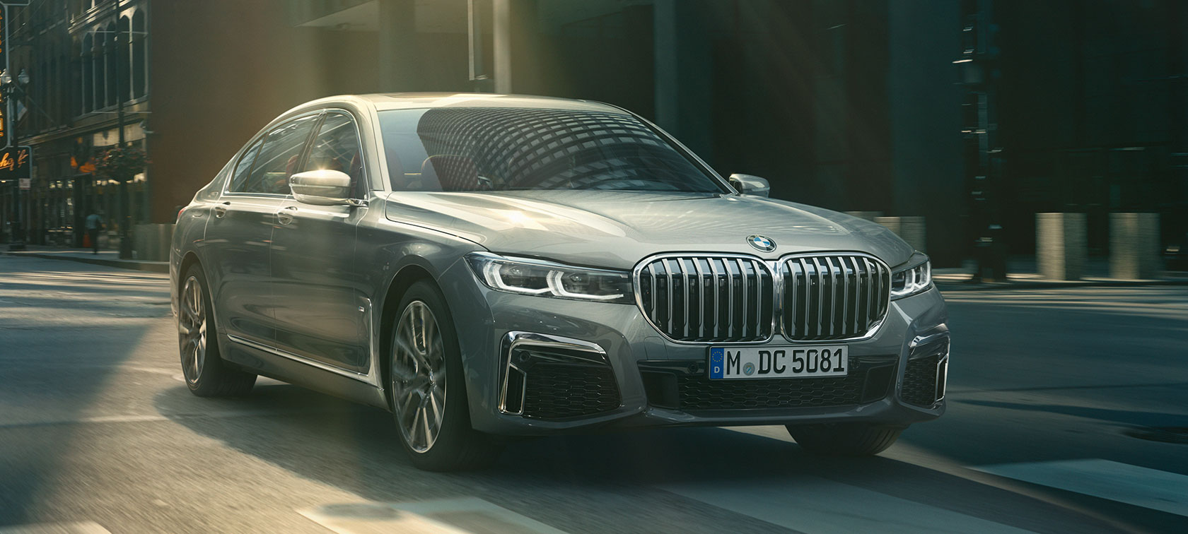 Vue de trois quarts avant d’une BMW Série 7 Berline grise en mouvement Vue de trois quarts avant d’une BMW Série 7 Berline grise roulant dans un décor urbain