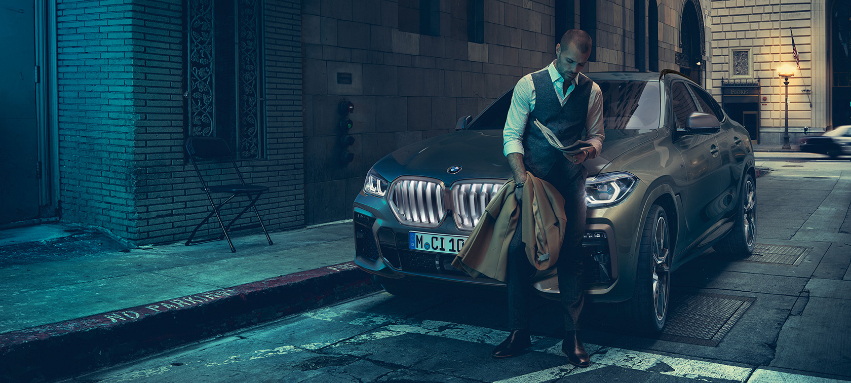 Homme en appui sur la BMW X6. Homme en appui sur la BMW X6 vue de profil devant un décor urbain.