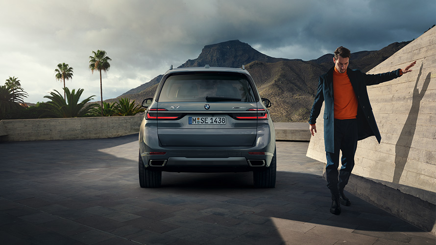 BMW X7 G07 LCI Design Pure Excellence Sparkling Copper Grey métallisé – vue arrière avec modèle sur la droite