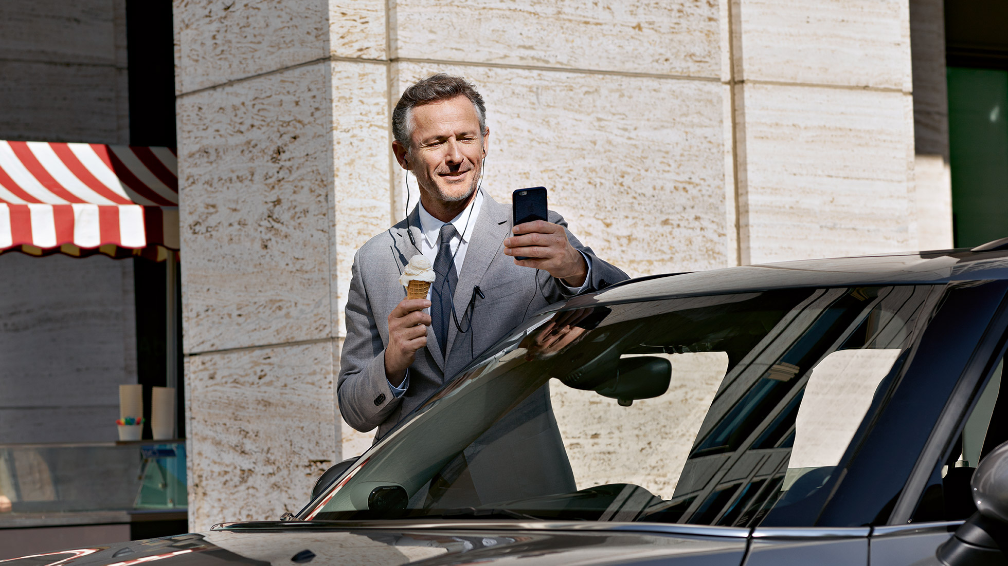 Service Après-vente entreprises BMW, contrôle de l’état des finances Service Après-vente entreprises BMW : Un homme mange une glace tout en contrôlant l’état de ses finances sur son smartphone