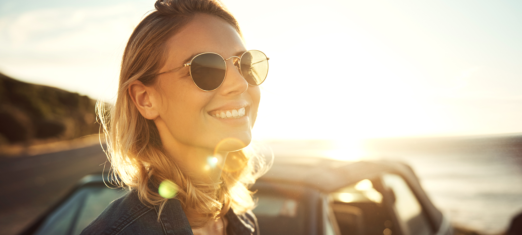 Accessoires d’origine BMW Accessoires d’origine BMW : une femme portant des lunettes de soleil sourit; en arrière-plan se dessine une BMW